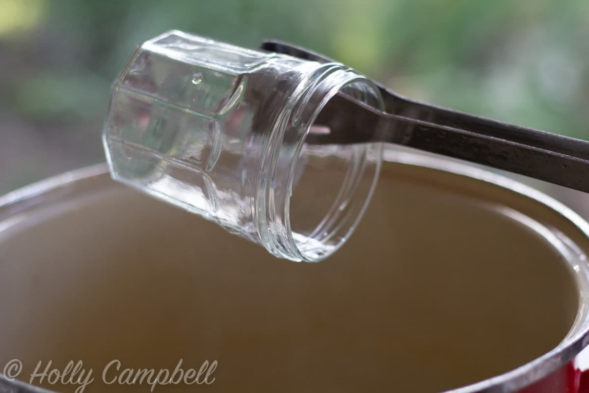 a tong holding a sterilized jar over a pot of biling water