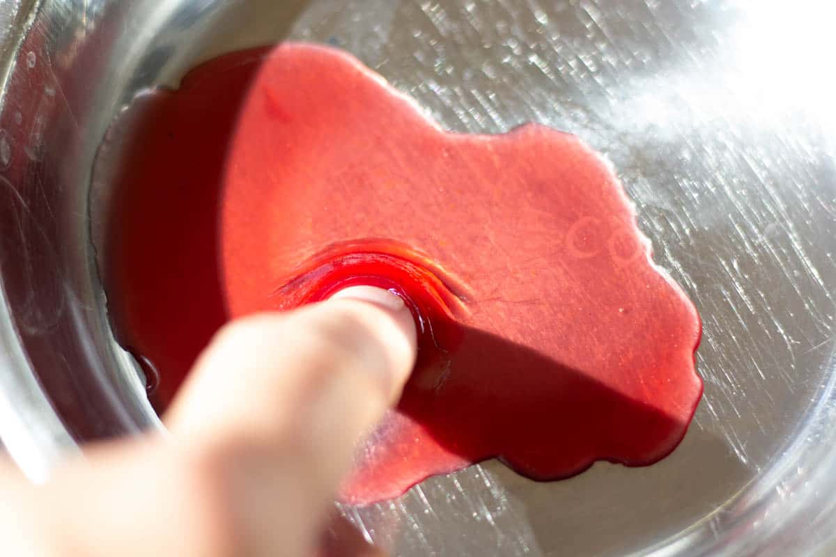 a finger pushing jelly in the saucer test. The jelly has reached the gel stage and wrinkles when pushed with finger