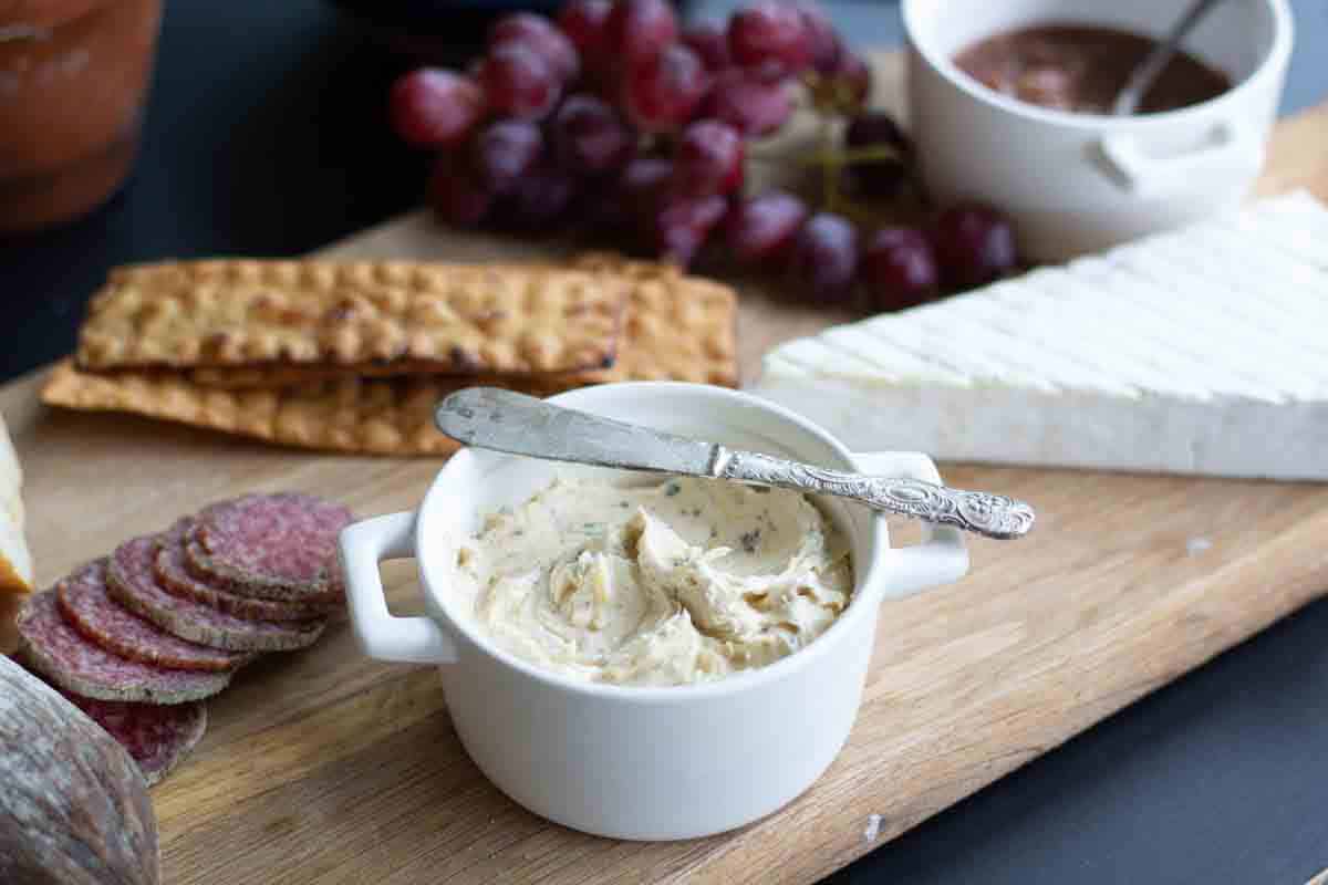 side view of bone marrow butter on a charcuteie board with cured meats, brie, crackers and red grapes