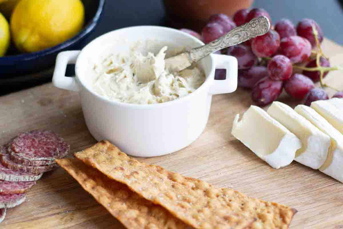 side angle view of a charcuterie board with bone marrow butter, crackers, salami, brie cheese,, grapes and lemons in the background