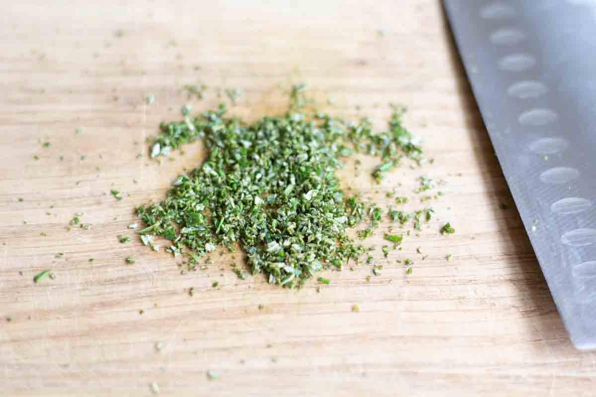 finely chopped rosemary on a wooden chopping board beside a sharp knife