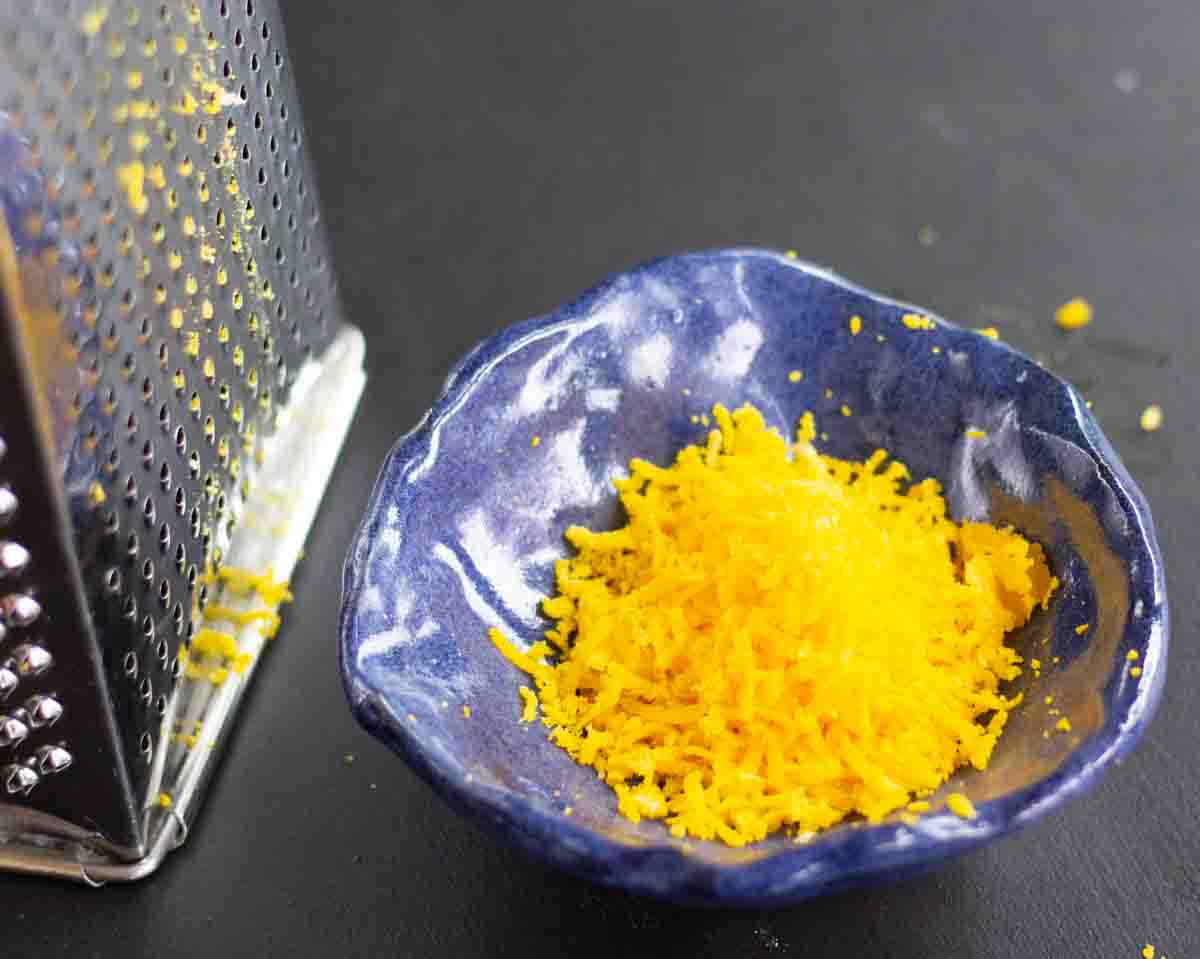 grated cured egg yolks in a dark blue ceramic bowl beside a grater