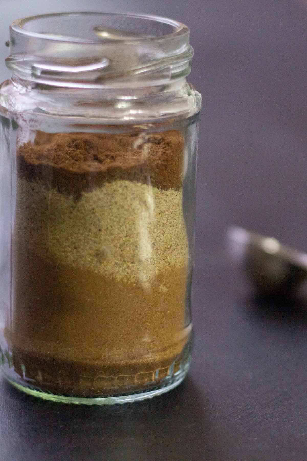 side view of a small glass jar filled with spices beside a measuring spoon