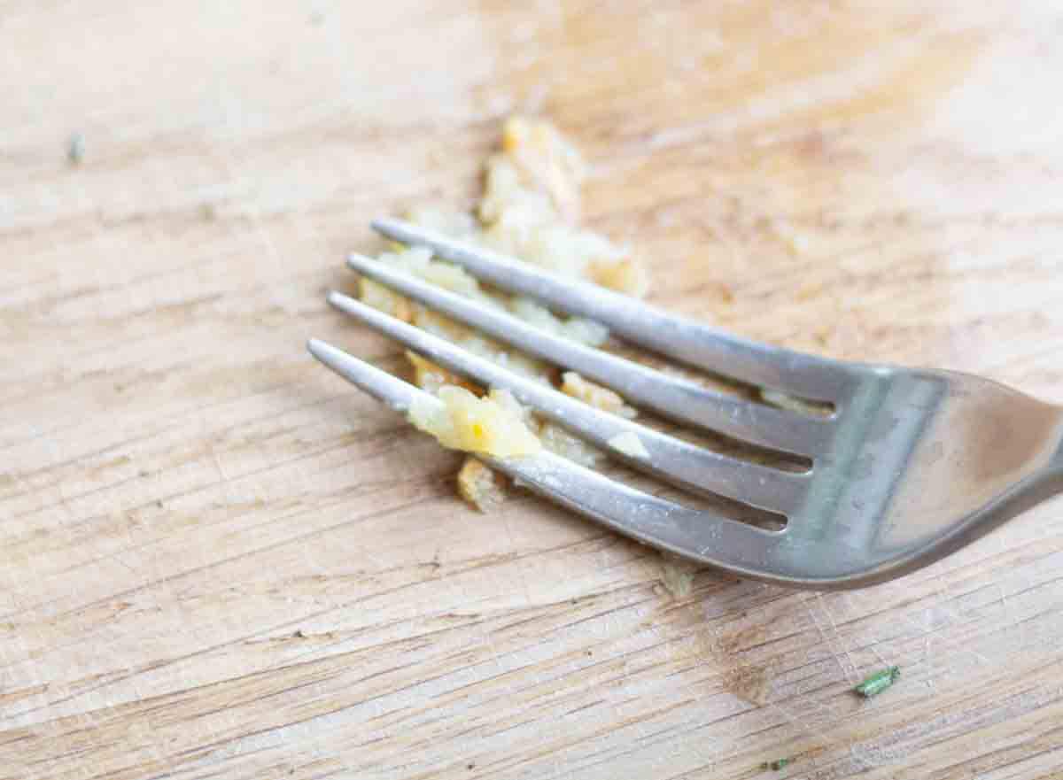 a fork mashing roasted garlic on a wooden chopping board