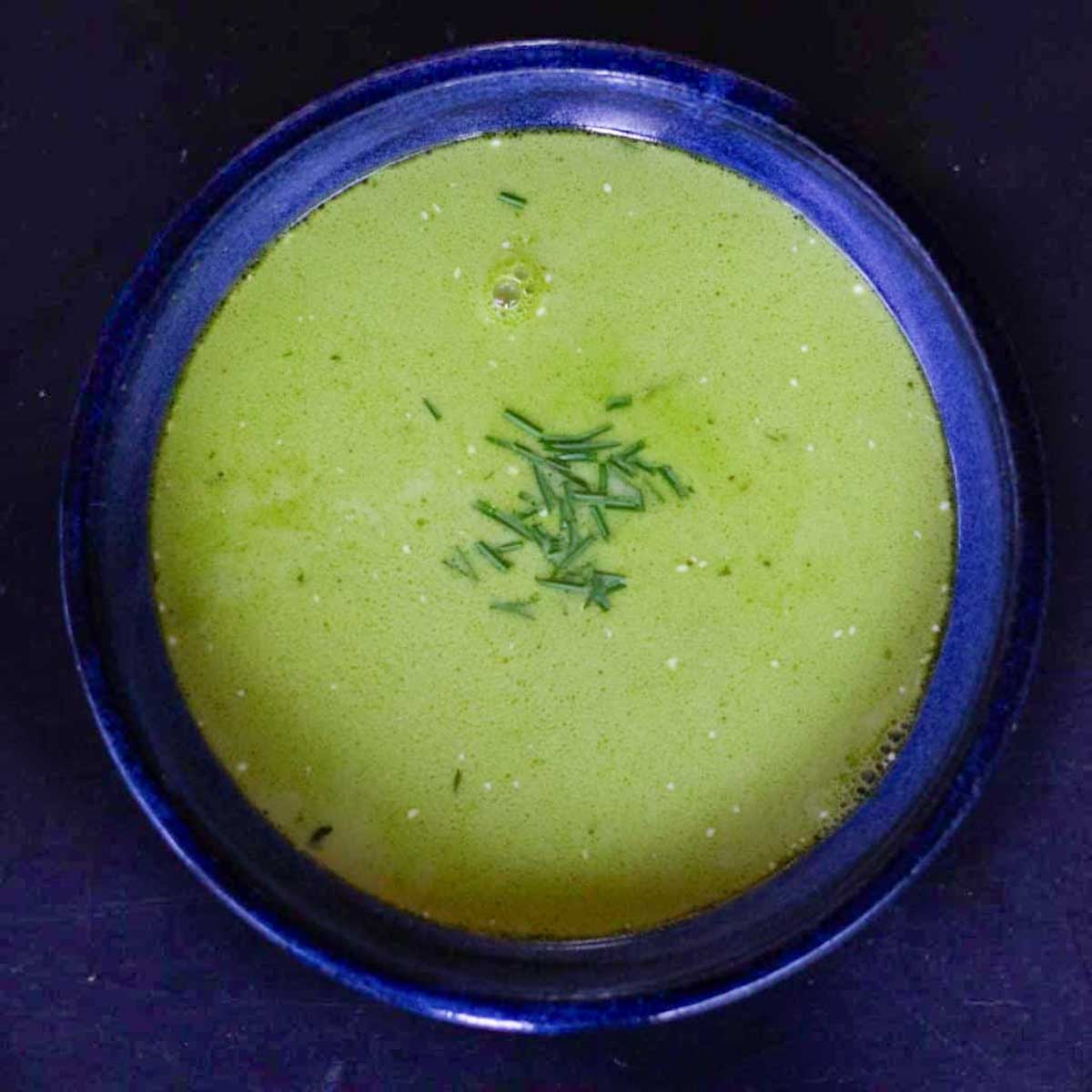 Over head view of a dark blue ceramic bowl of pea shoot soup garnished iwth choped chives
