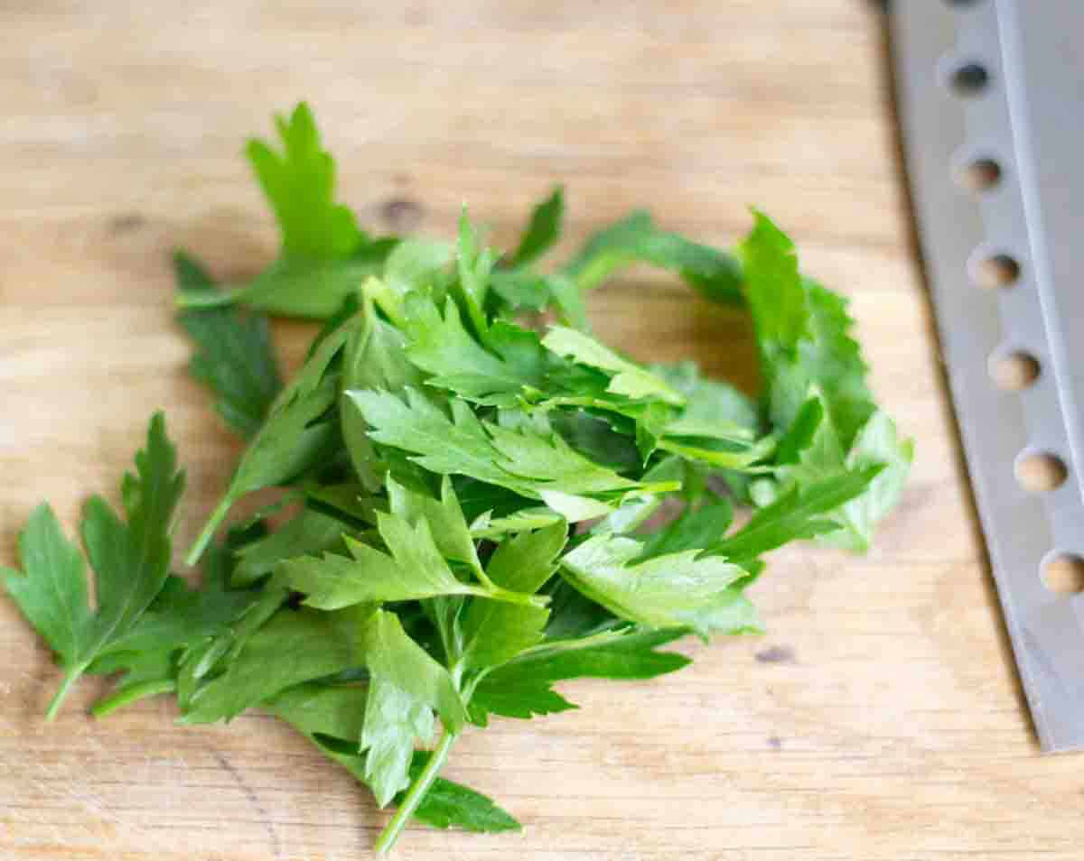 fresh parsley leaves on a wooden chopping board beside a sharp knife