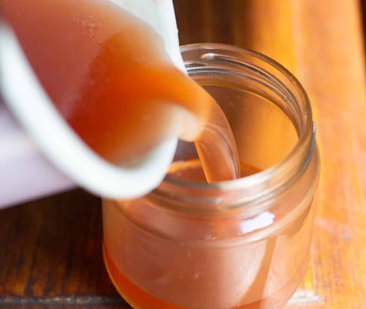 a small pot pouring liquid rowan berry jelly into a small glass jar