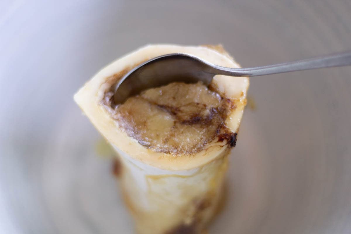 a spoon scooping bone marrow out of a roasted beef marrow bone
