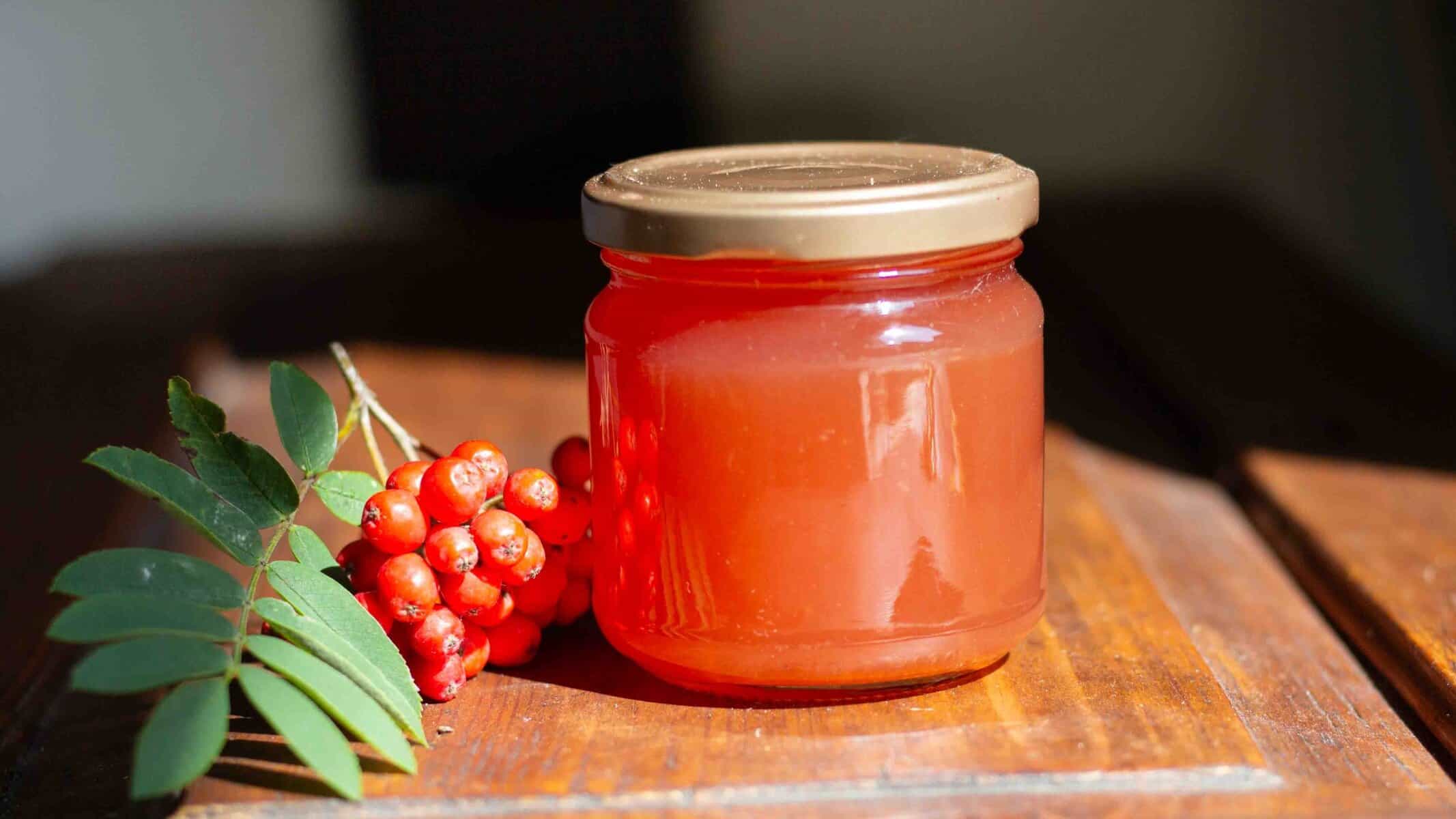 jar of rowanberry jelly beside fresh rowan berries and rowan tree leaves on a wooden table