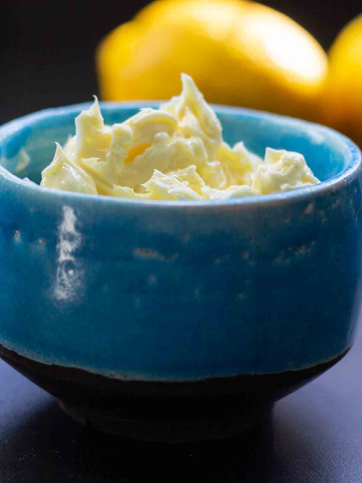 Whipped lemon butter in a cermic bowl with fresh lemons in the background