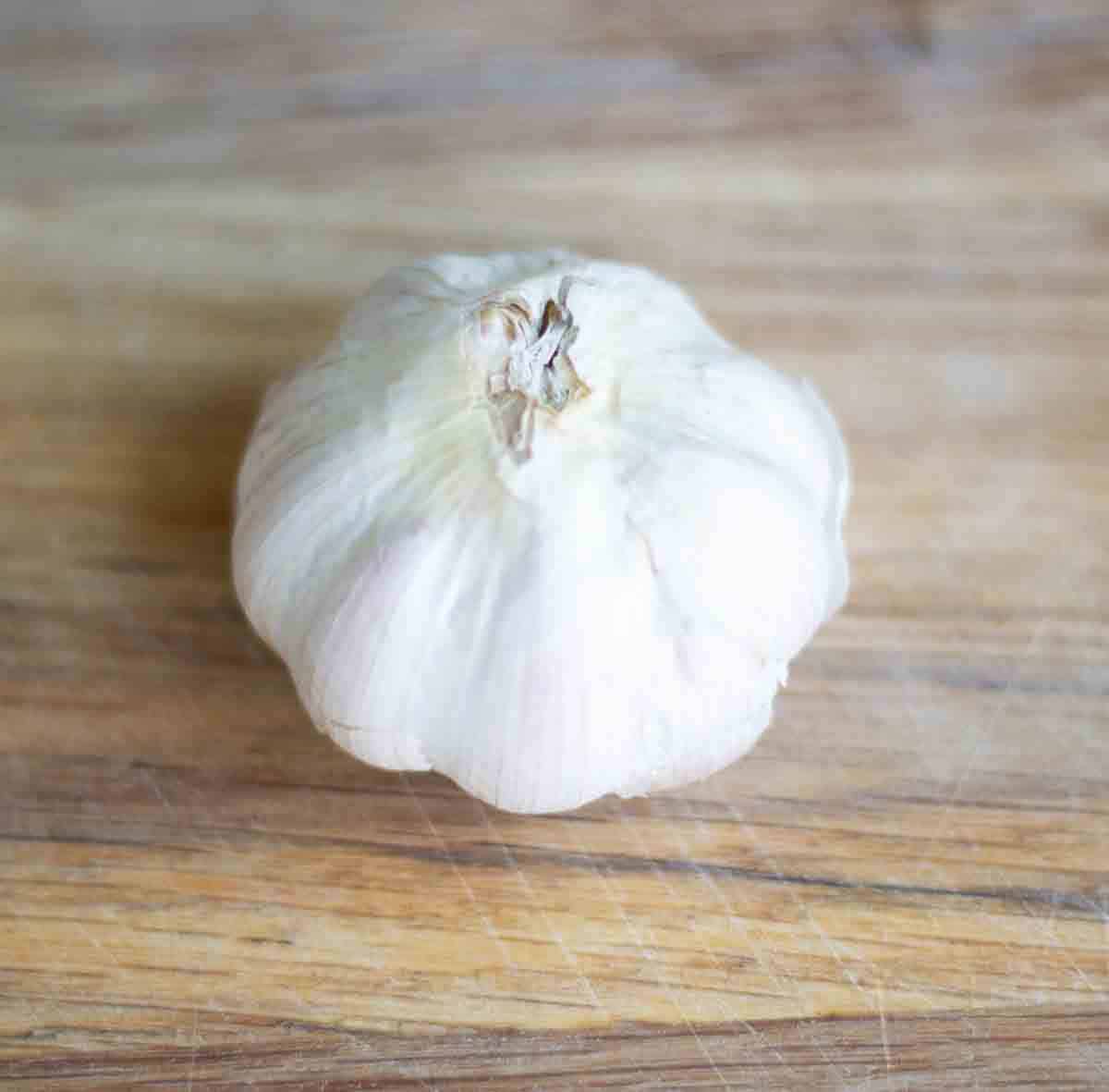 a whole head of garlic on a wooden chooping board